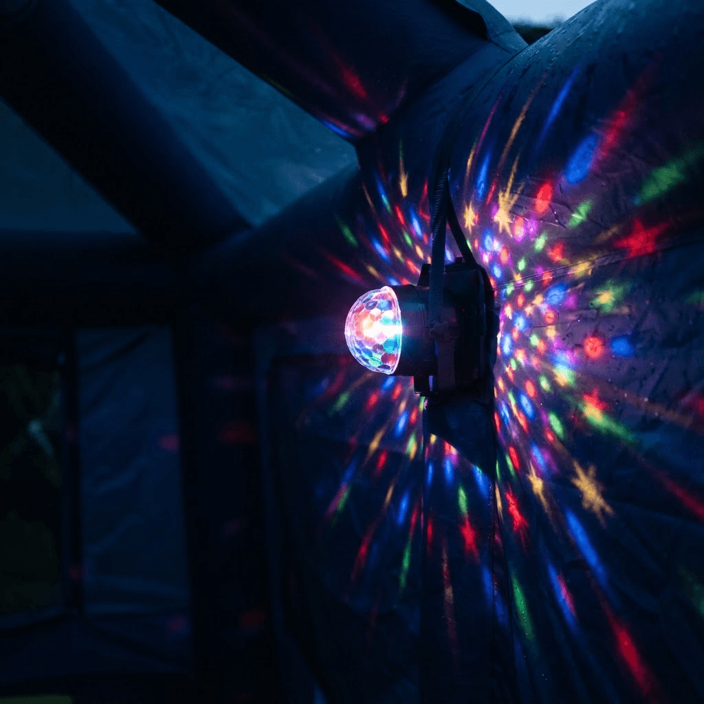 A multicolor disco light projector glowing against the dark fabric wall of the party dome at dusk